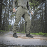 Henkilö pukeutuneena M-Tac-housuihin Aggressor Summer Flex metsässä, kevyet rip-stop-nylonkankaat, sopii kuumaan säähän ja ulkoiluun.