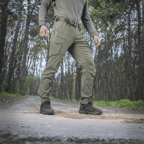 Henkilö pukeutuneena M-Tac-housuihin Aggressor Summer Flex metsässä, kevyet rip-stop-nylonkankaat, sopii kuumaan säähän ja ulkoiluun.