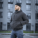 Mies pukeutuneena M-Tac Rubicon Jakke Gen. II -takkiin, kestävä ja lämmin bomber-takki modernin rakennuksen edessä.