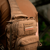 Mies ruskean laukun kanssa, jossa M‑Tac Patch Poland End-to-End 25x80 Cordura 500D:ssä, kiinnitetty tarralla. Näkyvissä laserkaiverrus.
