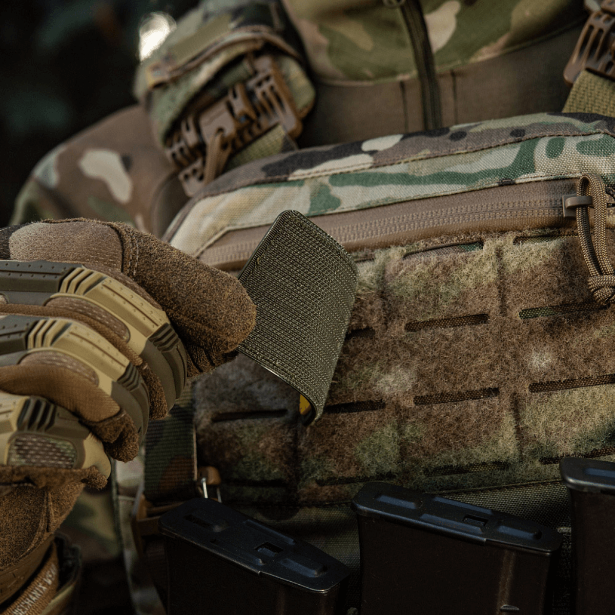 Maastopukuinen sotilas pitää M-Tac Patch Ukraine Flag -vaakunaa, kiinnitetty Velcrolla varusteeseen.